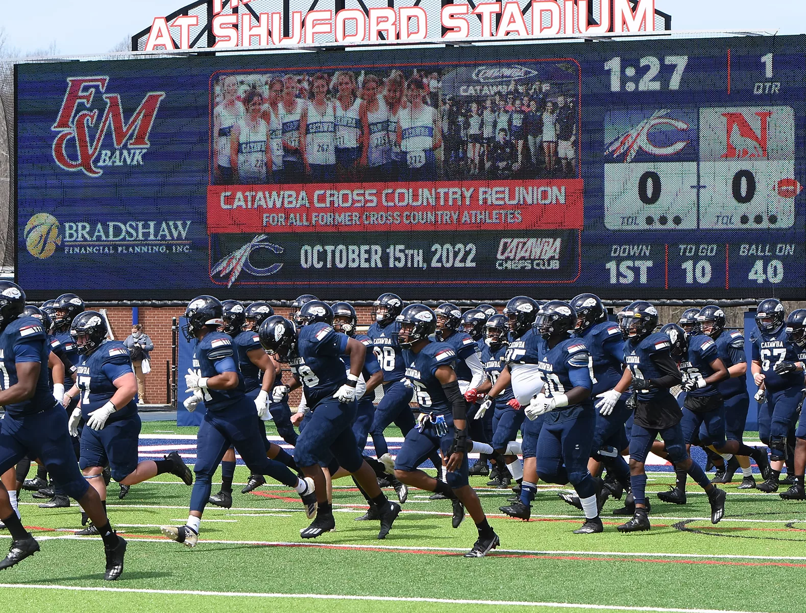 Football Players running in front of video scoreboard